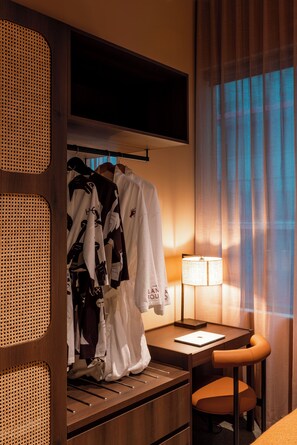 Ein Hotelzimmer mit einem Holztisch, einem Laptop, einer Lampe und einem Kleiderständer mit Bademänteln.