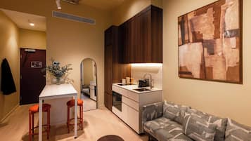 A compact living space with a kitchenette, a dining area with stools, a sofa, and a large abstract painting on the wall.