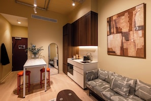 Un espacio habitable compacto con kitchenette, una zona de comedor con taburetes, un sofá y un cuadro abstracto grande en la pared.