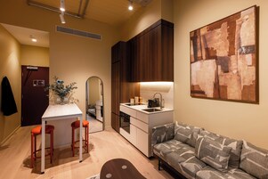 A compact living space with a kitchenette, a dining area with stools, a sofa, and a large abstract painting on the wall.