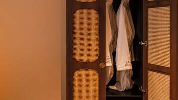 Een houten garderobe met een deur van geweven materiaal, waarin kleding hangt en een televisie staat.