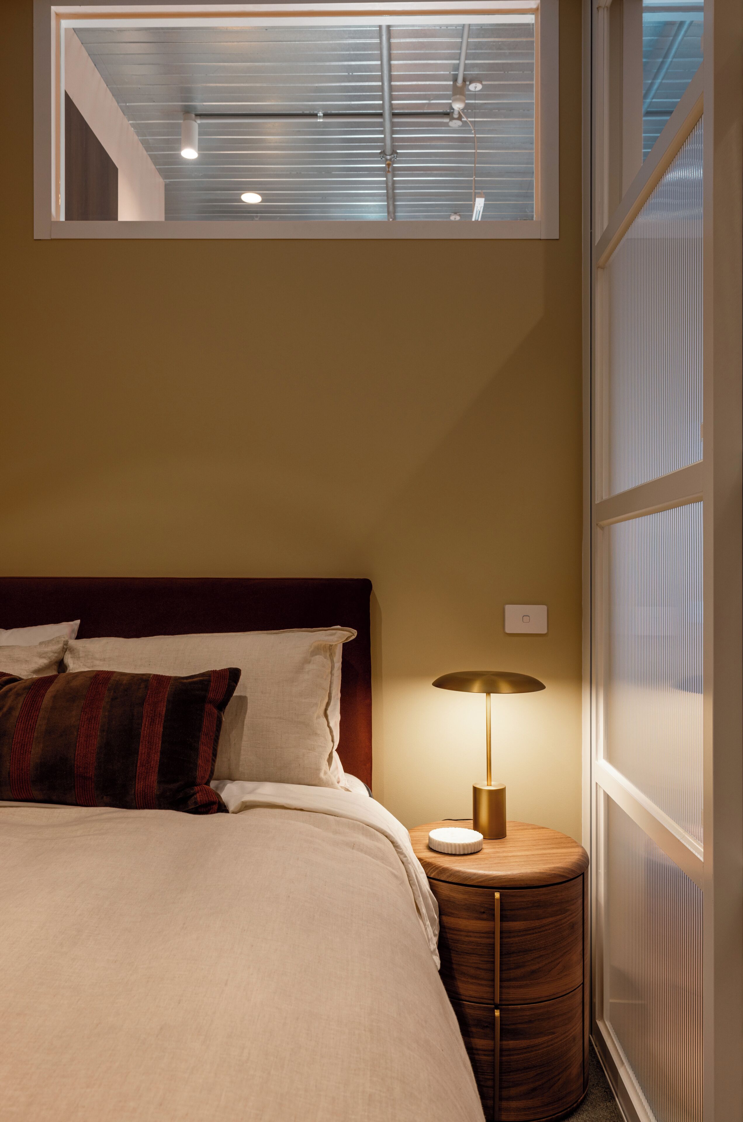 A bedroom with a bed, a bedside lamp, and a window with blinds.