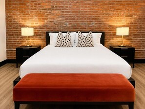 A bed with white bedding, two black nightstands with lamps, a brick wall, and a wooden floor. - Brick & Bed - Historic Loft/Walk to Stadium/Arch (St. Louis)
