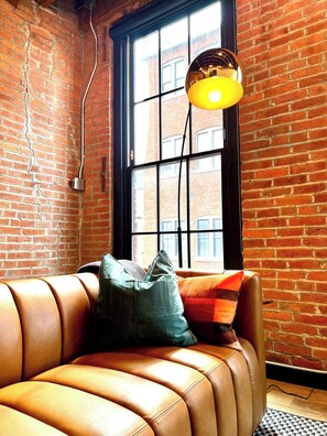 A leather sofa with cushions, a hanging lamp, and a brick wall with a window. - Brick & Bed - Historic Loft/Walk to Stadium/Arch (St. Louis)