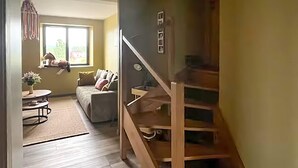 Una escalera que lleva a un segundo piso, una sala de estar con un sofá y una mesita, y un ventanal con vistas a la vegetación.