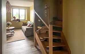 Eine Treppe führt zu einer zweiten Etage, einem Wohnzimmer mit Sofa und kleinem Tisch sowie einem Fenster mit Blick ins Grüne.