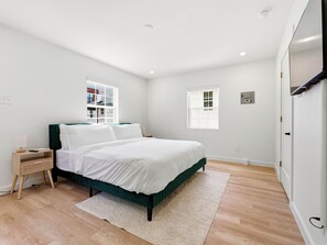 Ein Schlafzimmer mit Bett, Nachttisch und zwei Fenstern.