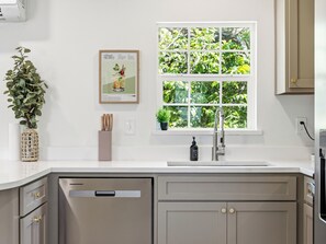 Eine Küche mit Fenster, einem Blumentopf, einem gerahmten Bild und einem Spülbecken.