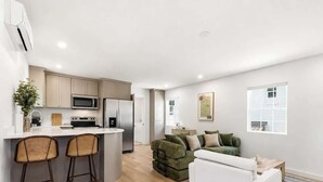Eine moderne Küche mit Kochinsel, Barhocker, einem grünen Sofa und einem weißen Sessel.