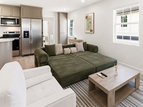 Eine moderne Küche mit Edelstahlgeräten, einem grünen Sofa, einem weißen Sessel und einem Holztisch.