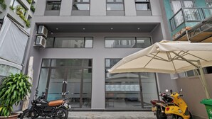 Un edificio de varios pisos con entrada central, unidades de aire acondicionado y plantas en macetas.