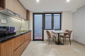 A modern kitchen with wooden cabinets, a built-in stove, and a dining area with a table and chairs. - Hampton Danang Central Apartment (Son Tra)