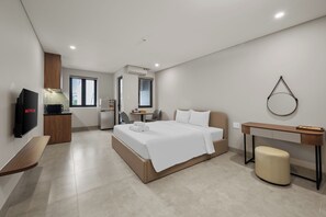 Una camera d'albergo moderna con un letto, un comodino, una TV e una scrivania con una sedia.