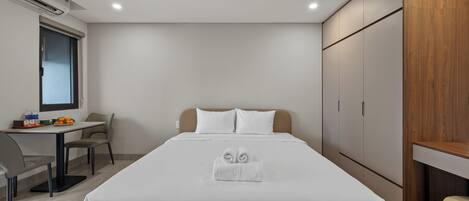 A hotel room with a bed, a desk, a chair, and a wardrobe.