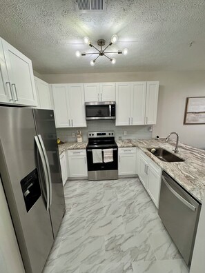 A modern kitchen with white cabinets, stainless steel appliances, a marble floor, and a ceiling light fixture. - Beautiful 2 bedroom/2 bath condo in Santa Rosa Beach (Santa Rosa Beach)