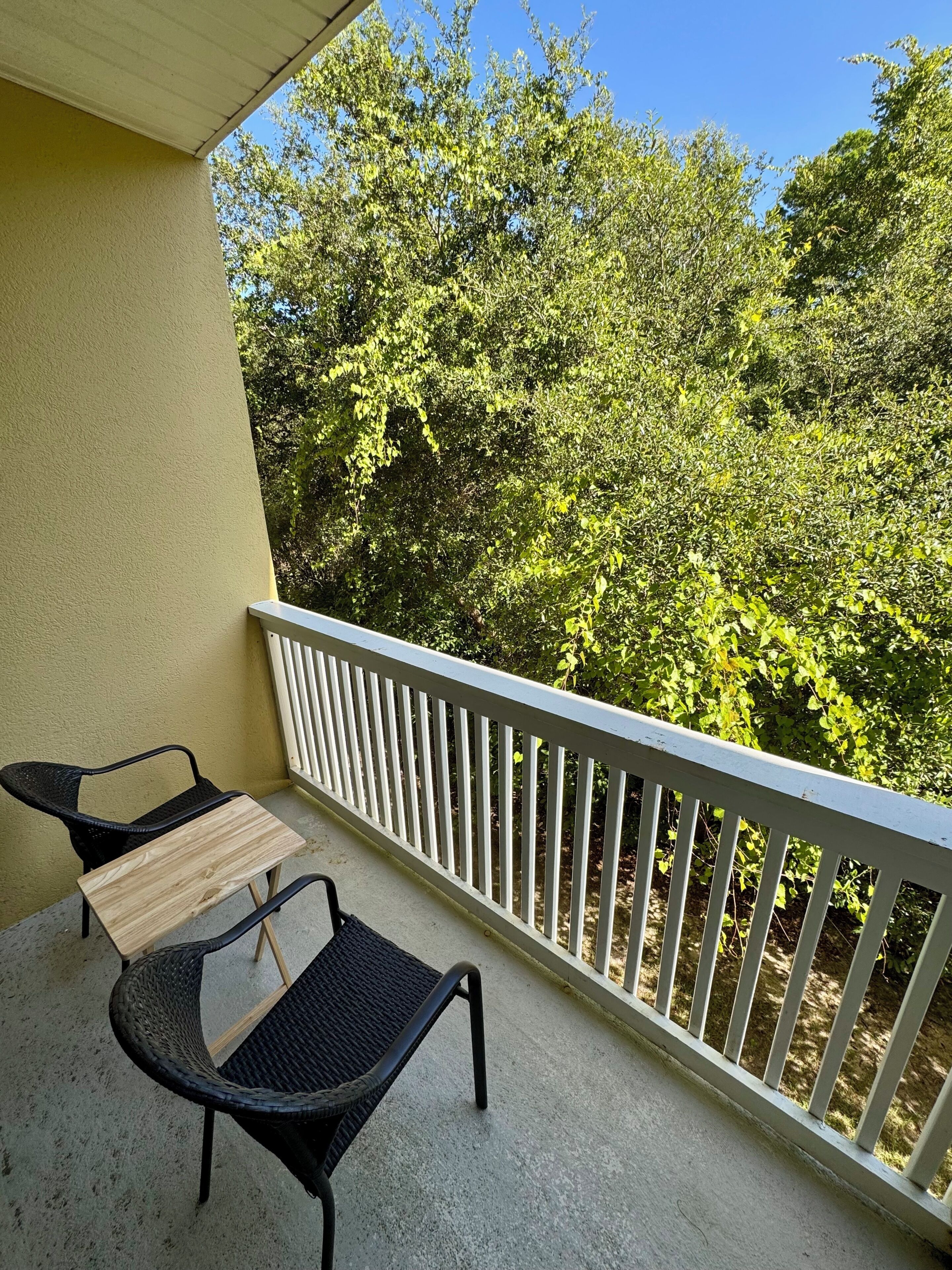 A balcony with a white railing, two wicker chairs, and a small wooden table.