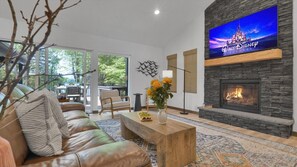 A living room with a stone fireplace, leather sofa, and a flat-screen TV displaying Walt Disney Pictures. - Waterfront Paradise | Sauna, Hot Tub, Fire Pit, Private Dock & Water Crafts (Pocono Summit)