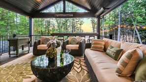 A covered outdoor seating area with wicker furniture, a glass coffee table, and a view of the forest. - Waterfront Paradise | Sauna, Hot Tub, Fire Pit, Private Dock & Water Crafts (Pocono Summit)
