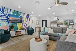 Ein modernes Wohnzimmer mit einem großen abstrakten Gemälde, einem grauen Sofa, einem türkisfarbenen Sessel und einem weißen Couchtisch.