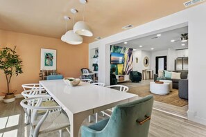 Ein modernes Wohnzimmer mit einem weißen Esstisch, blaugrünen Stühlen, einer Couch und einem Couchtisch.