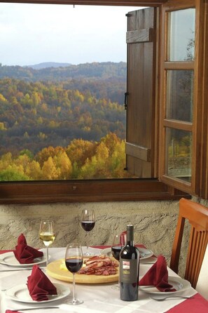Ein Tisch ist mit Tellern, Gläsern und einer Flasche gedeckt, mit Blick auf herbstliche Bäume durch ein Fenster.