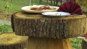Ett rustikt träbord med en tallrik mat, en flaska och ett glas vin, placerat utomhus med en skog i bakgrunden.