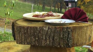 A rustic wooden table with a plate of food, a bottle, and a glass of wine set outdoors with a forest backdrop.