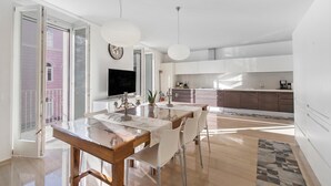 Een moderne keuken met witte kasten, een groot raam en een eethoek met een houten tafel en stoelen.