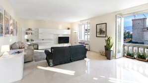 Een moderne woonkamer met een bank, televisie en balkon met uitzicht op een toren.