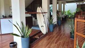 Un pasillo con suelo de madera, plantas en macetas y tablas de surf apoyadas contra la pared.