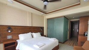 Una habitación de hotel con cama, escritorio, silla, armario y ventilador de techo.