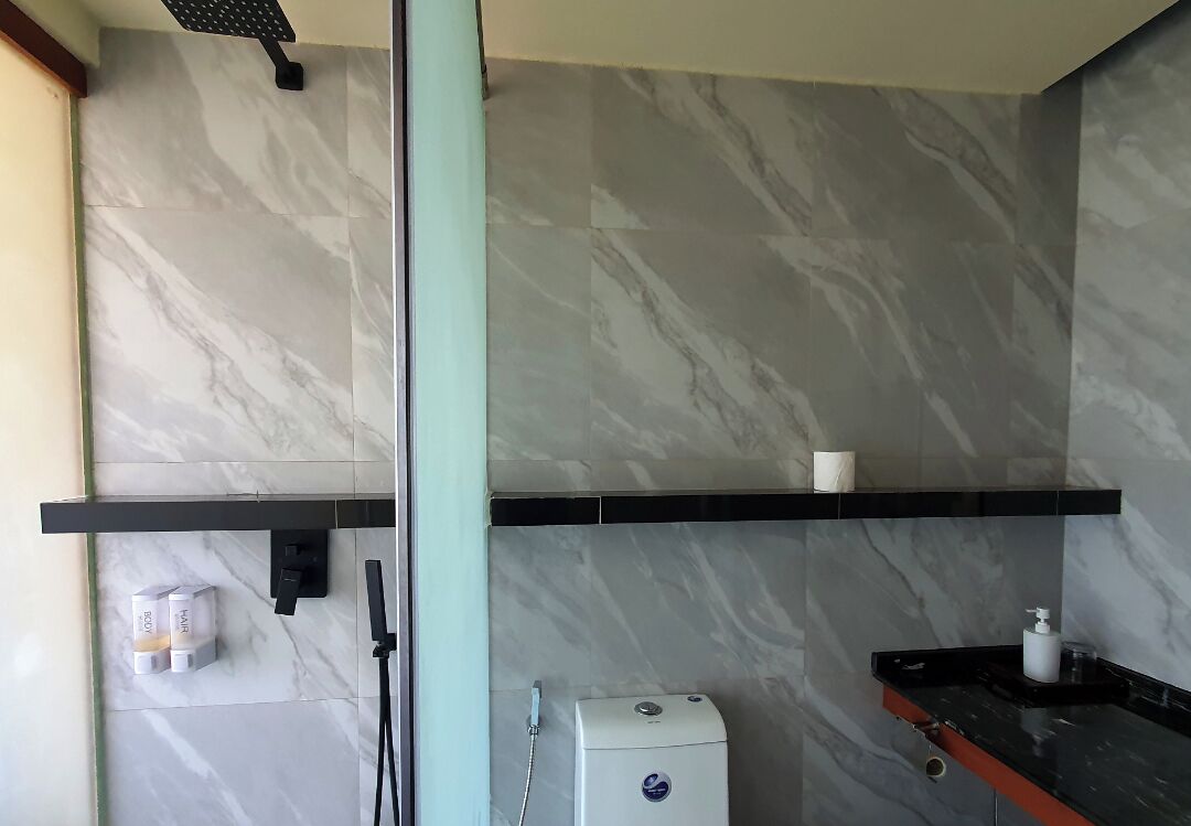 Ein Badezimmer mit Marmorwänden, einer Dusche, einer Toilette und einem Ablagefach mit Toilettenartikeln.