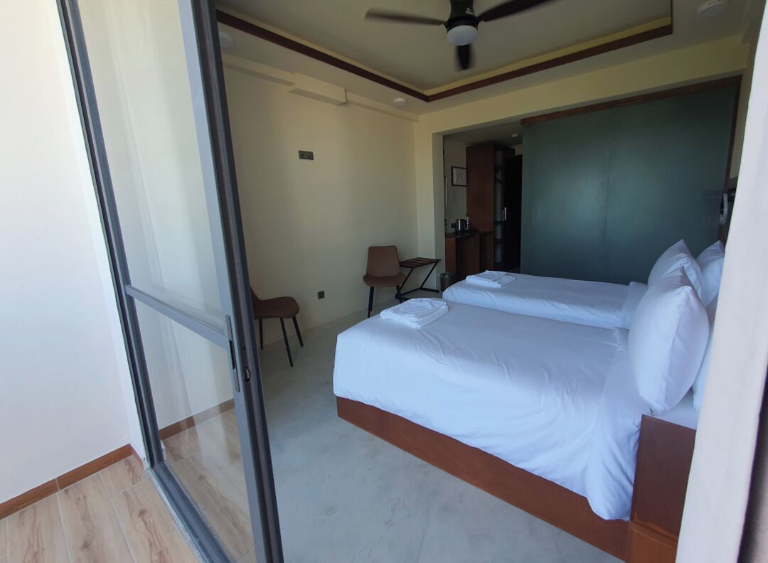 A hotel room with two beds, a ceiling fan, a chair, and a kitchenette in the background.