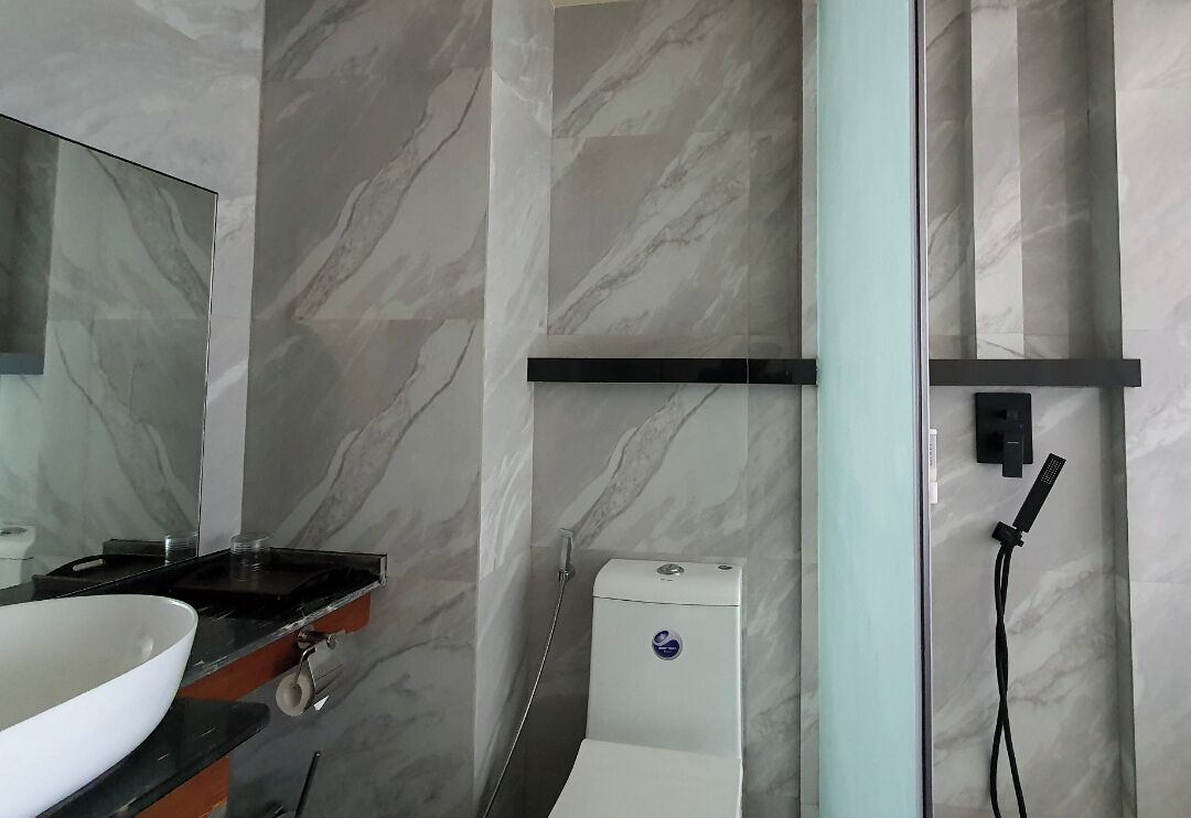 Un baño con pared de mármol, un lavabo blanco, un espejo y una zona de ducha.