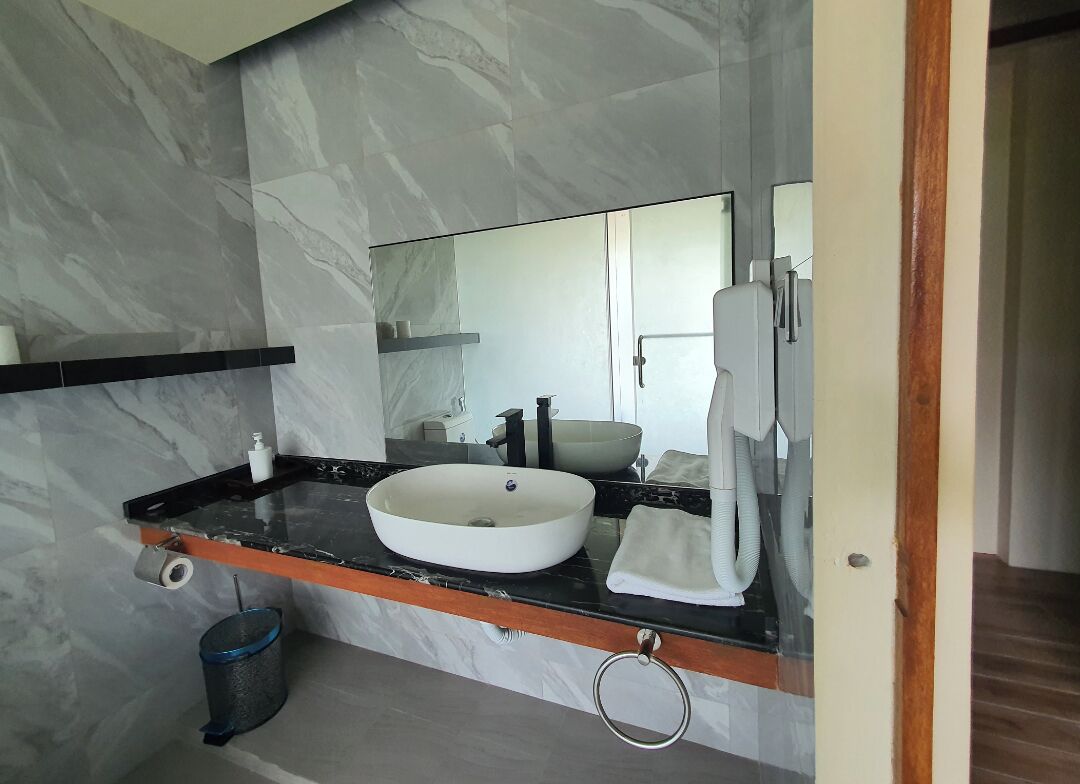 A modern bathroom with a marble wall, a black countertop, a white sink, a mirror, a towel, and a trash can.