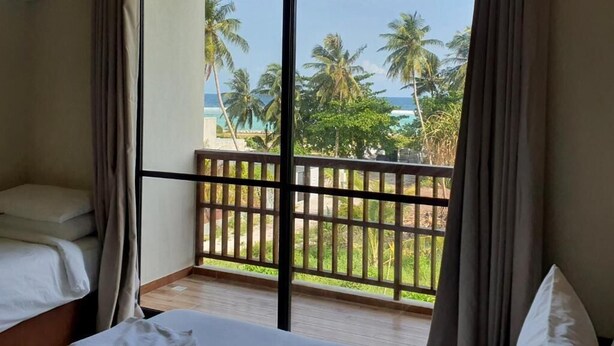 Habitación de hotel con balcón, una cama y vistas a palmeras y al océano.