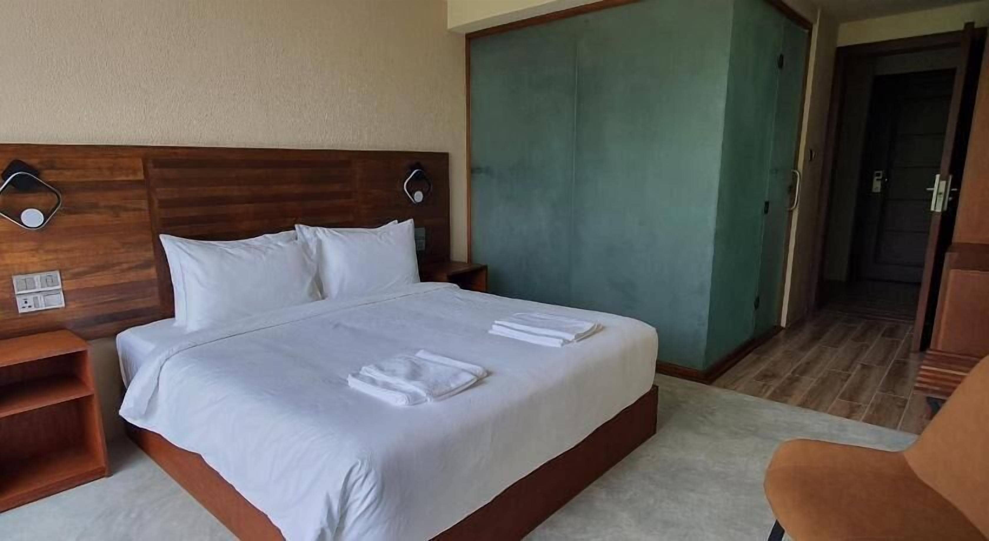 Una habitación de hotel con cama, mesitas de noche, armario y una silla.