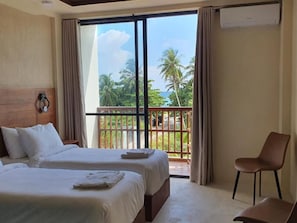 Habitació d'hotel amb dos llits, una cadira i un balcó que ofereix vistes a palmeres i l'oceà.