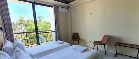 A hotel room with two beds, a ceiling fan, a balcony with a view of palm trees, and a small table.