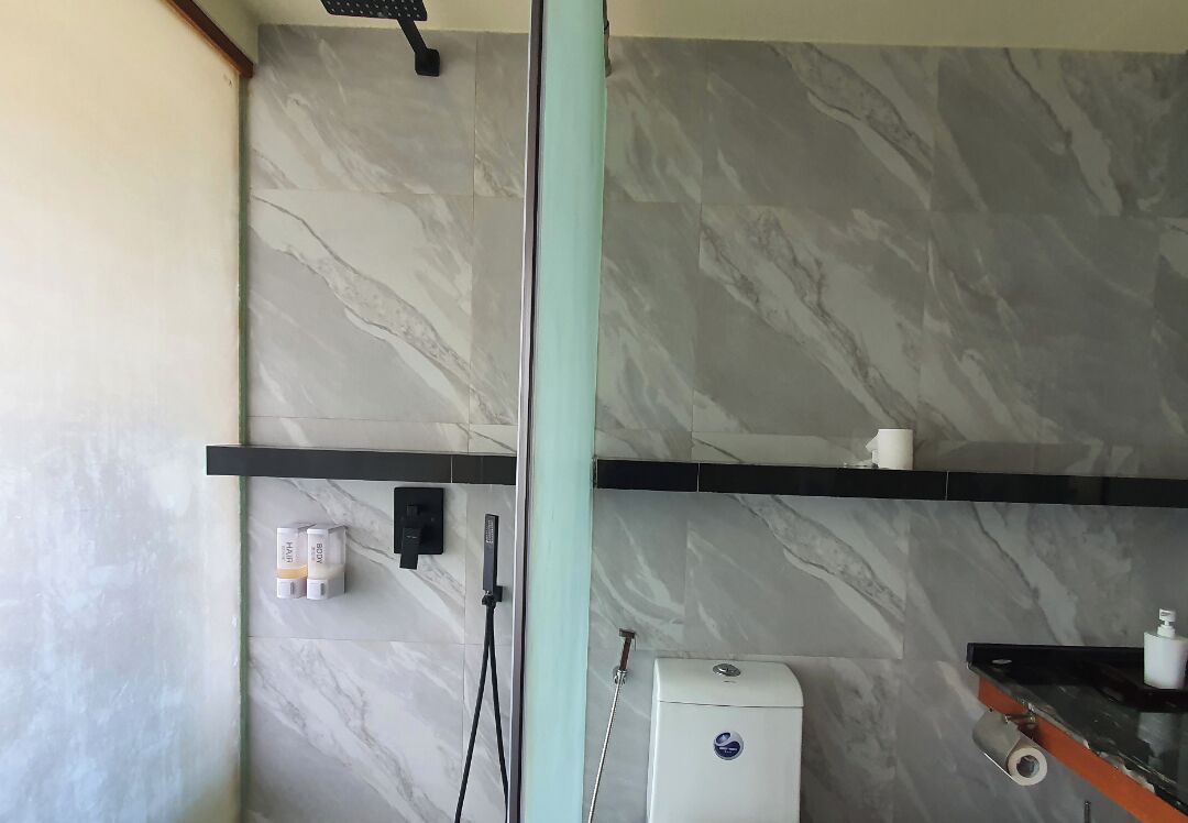 A bathroom with marble walls, a shower, a toilet, and a shelf with toiletries.