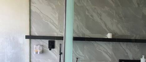 A bathroom with marble walls, a shower, a toilet, and a shelf with toiletries.