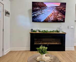 Un salon doté d’un téléviseur à écran plat fixé au mur, d’une cheminée en dessous et d’une petite table sur laquelle est posée une plante.