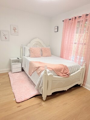 Une chambre à coucher avec un lit, une table de chevet, un tapis rose et une fenêtre avec des rideaux roses.