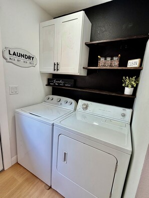 A laundry area with two washing machines, a cabinet, and a shelf with jars and a potted plant. - Lovely 3-bedroom house with AC in vibrant Dallas (Dallas)