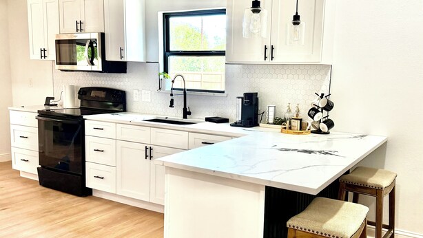 A modern kitchen with white cabinetry, a black stove, a large island with stools, and pendant lighting.