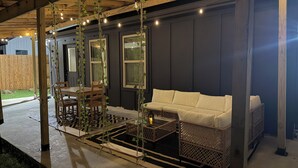 An outdoor patio with a wooden table and chairs, a white sofa, and hanging string lights.
