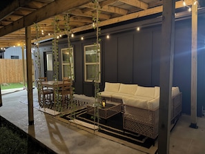 An outdoor patio with a wooden table and chairs, a white sofa, and hanging string lights.