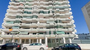 Un edificio de varios pisos con balcones, entrada con portón y coches estacionados.