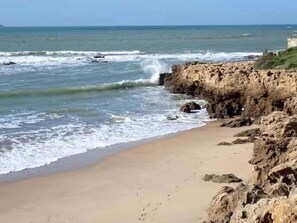A beach with a rocky shoreline and waves crashing onto the sand. - GuestReady - Fuentebravia with terrace and pool (El Puerto de Santa María)