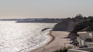 Vista costera con playa, un acantilado y el perfil distante de una ciudad.